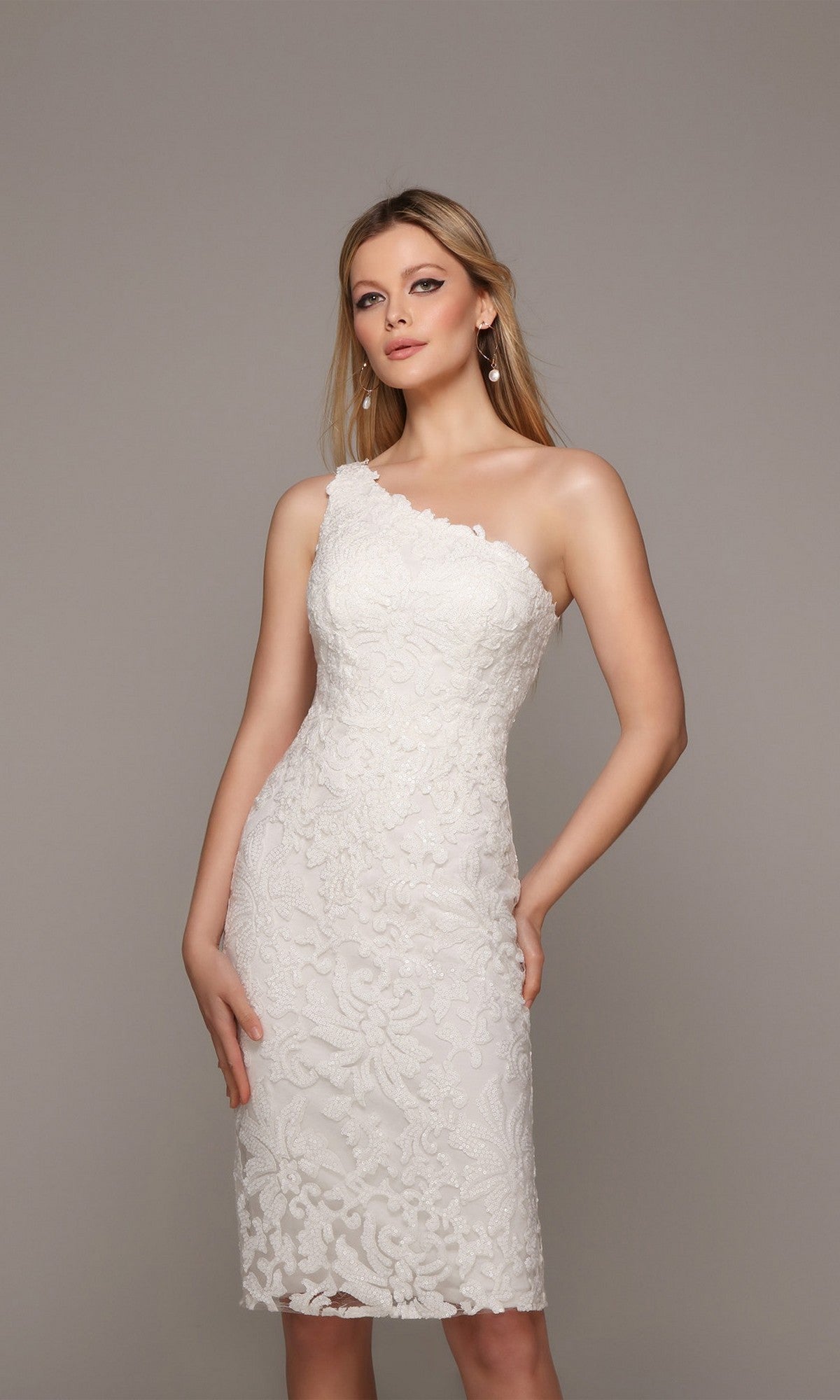 A woman stands against a plain grey background wearing the Alyce 70029 knee-length ivory party dress, featuring floral patterns and a one-shoulder design.